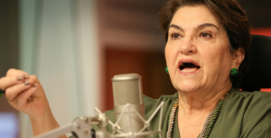 A Ministra das Mulheres, Márcia Lopes, gesticula enquanto fala ao microfone; imagem ilustra a proposta do governo de incluir temas sociais no ensino básico.