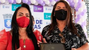 A ex-prefeita Moema Gramacho e uma secretária, ambas de máscara, segurando um tablet durante evento oficial; imagem ilustra a Operação Nota de Conceito da PF.