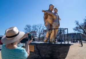 Mulher com chapéu de palha fotografa estátua dourada de Donald Trump e Jeffrey Epstein na pose de Titanic instalada em frente ao Capitólio em Washington.