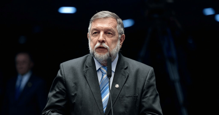 Fotografia do Senador Flávio Arns, de terno escuro e gravata azul, discursando ao microfone em plenário.