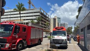 Um caminhão vermelho do Corpo de Bombeiros e uma ambulância branca do SAMU estacionados na rua em frente a um edifício em Salvador, com equipes de resgate na calçada.