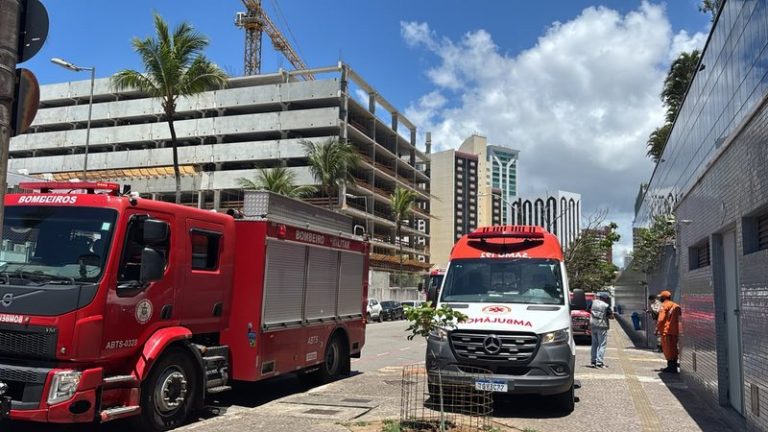 Um caminhão vermelho do Corpo de Bombeiros e uma ambulância branca do SAMU estacionados na rua em frente a um edifício em Salvador, com equipes de resgate na calçada.